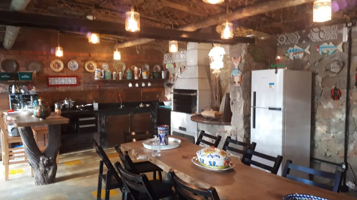 Cozinha comunitária com fogão, churrasqueira, geladeira e mesa grande de madeira